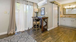 A well-lit room with a wooden floor, a desk with a chair, a window with sheer curtains, and a kitchen area with a sink and cabinets. - Elegant Napa Escape Walk to Wineries & Dining (Napa)