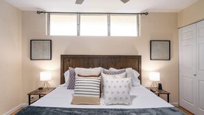 Een slaapkamer met een groot bed, twee nachtkastjes met lampen, een houten hoofdbord en twee ingelijste foto's aan de muur.