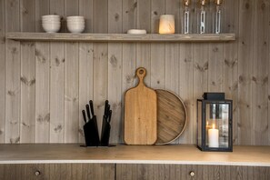 Un plan de travail de cuisine avec une planche à découper en bois, un range-couteaux, une lanterne et une étagère avec des bols et une bougie.