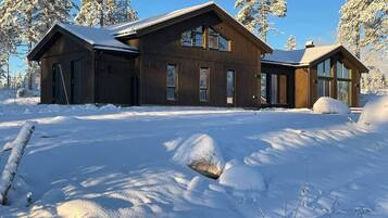 A wooden cabin with large windows, surrounded by snow-covered trees.