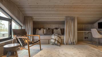 A cozy cabin interior with a wooden ceiling, a sofa with cushions, a chair, a TV, and a large window.