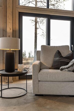 A modern living room with a sofa, a lamp, and a view through large windows. - Luxury Trysil Chalet: Hot Tub & Sauna (Trysil)