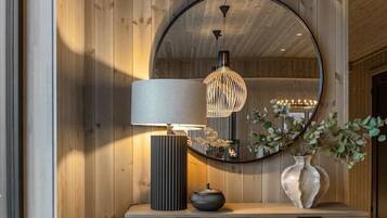 A room with wooden panel walls, a round mirror, a lamp, and a vase with plants.
