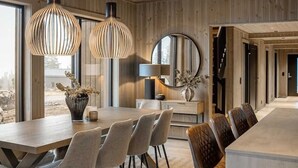 A modern interior with a wooden ceiling, a dining area with a long table and chairs, and pendant lighting.