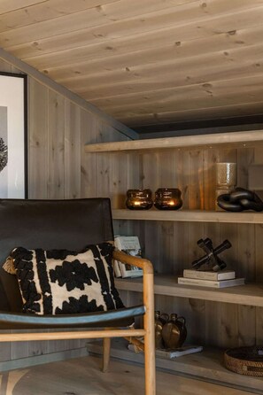 A wooden interior with a chair, shelves with books and decorative items, and a framed picture on the wall. - Luxury Trysil Chalet: Hot Tub & Sauna (Trysil)
