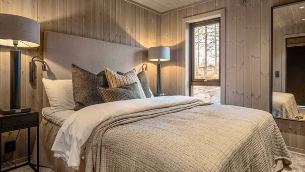 A wooden-paneled bedroom with a bed, bedside lamps, and a window.