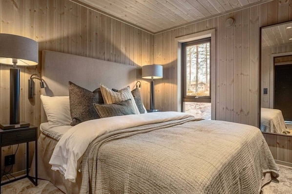 A wooden-paneled bedroom with a bed, bedside lamps, and a window.