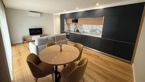 Een moderne keuken met donkere kastjes, een marmeren spatwand, en een eetgedeelte met een ronde tafel en vier stoelen.