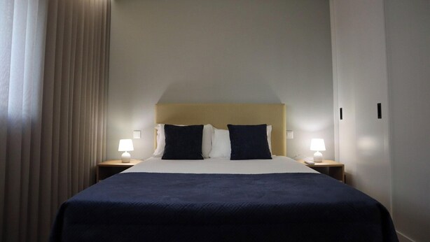 Een hotelkamer met een bed, twee bedlampen, een hoofdbord en een gordijn.