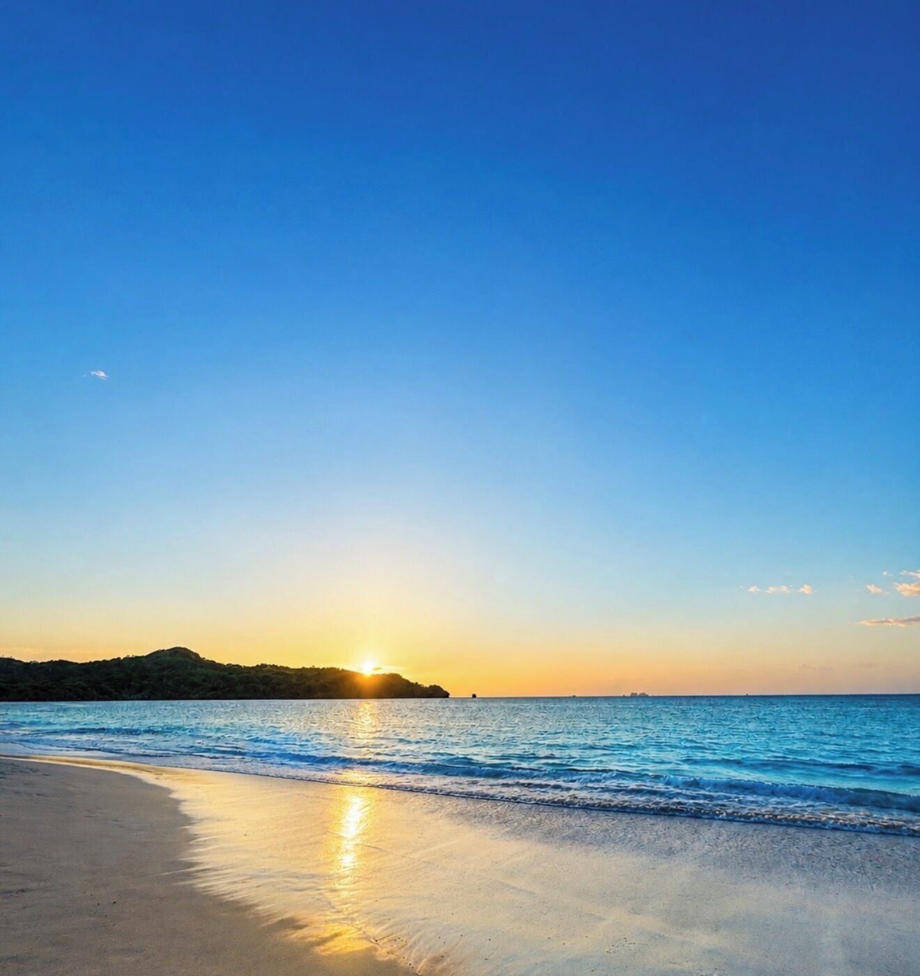 A beach with a sunset, calm sea, and a distant landmass.