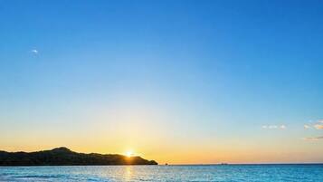 A beach with a sunset, calm sea, and a distant landmass.