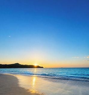 Una playa con un atardecer, mar tranquilo y una masa de tierra distante.