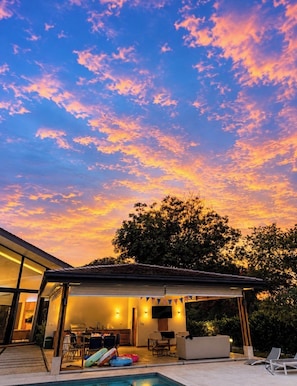 A modern outdoor living area with a pool, a covered patio, and a view of the sky.