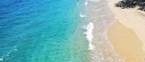 A beach with clear turquoise water, sandy shore, and trees.