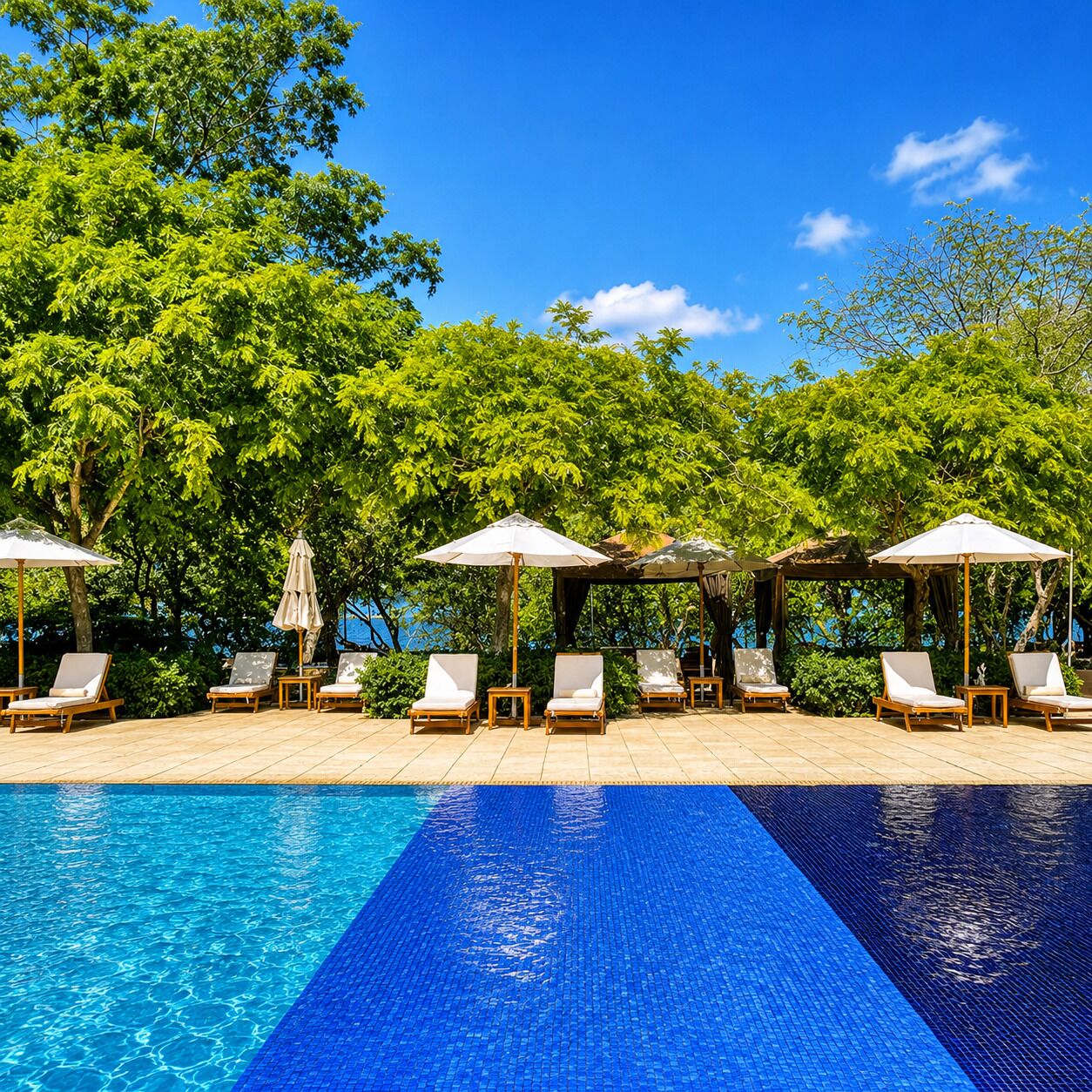 A poolside area with lounge chairs and umbrellas, surrounded by lush greenery.