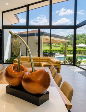 A modern interior with a dining area, large windows, and a view of a pool and greenery.