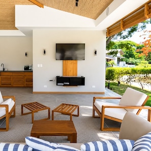 A modern living room with a flat-screen TV, wooden furniture, and a view of a garden.