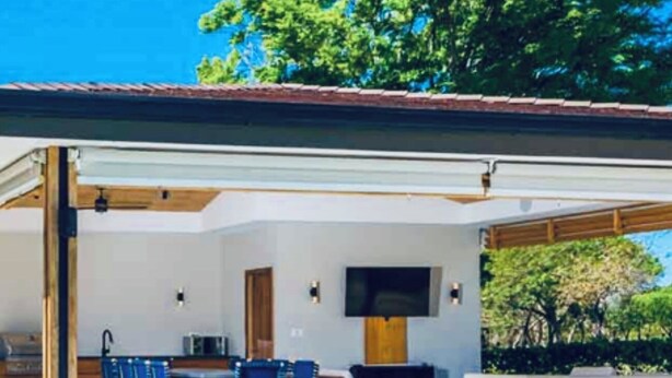 Un área de piscina moderna al aire libre con un espacio de estar cubierto y una piscina de color azul cristalino.