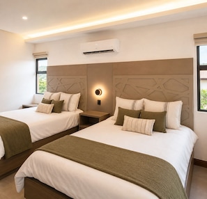 A hotel room with two beds, a wall-mounted air conditioner, a bedside table with a lamp, and a window with a view.