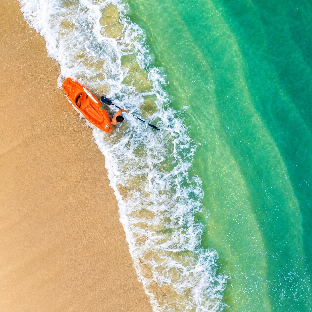 An aerial view of a beach with clear turquoise water and a sandy shore.