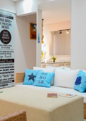A modern living room with a sofa, a coffee table, and a dining area with chairs and a table. - Apartment with a gourmet balcony, 150 m from Enseada Beach (Guarujá)
