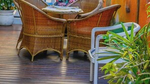 A wicker outdoor seating area with two chairs and a table, surrounded by potted plants and a decorative wall. - Apartment with gourmet balcony, 150m from Enseada beach. (Guarujá)
