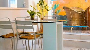 A modern dining area with a glass table, metal chairs, and a hanging light fixture. - Apartment with gourmet balcony, 150m from Enseada beach. (Guarujá)