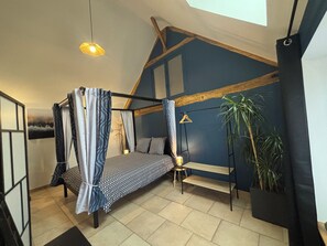 A bedroom with a bed, a hanging light, a plant, and a window. - Le Merisier (Épieds)