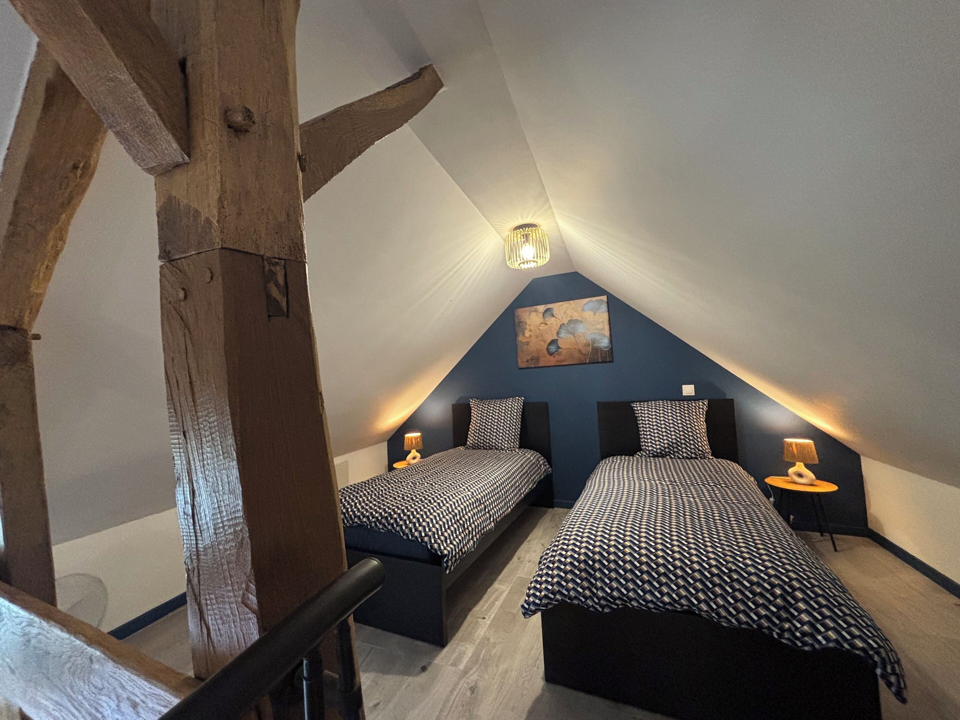 Een slaapkamer met twee bedden, een schuine plafond en een schilderij aan de muur.