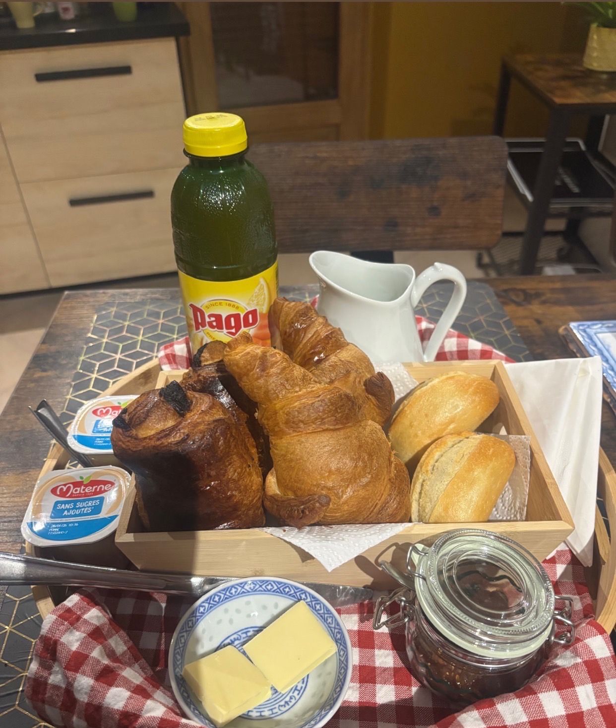 Un plateau de petit-déjeuner avec des croissants, une bouteille de Dango, un pichet, un bol de beurre et un pot de confiture.