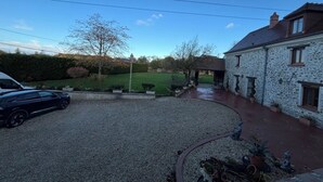 A gravel driveway leading to a stone building with a covered patio area. - Le Merisier (Épieds)