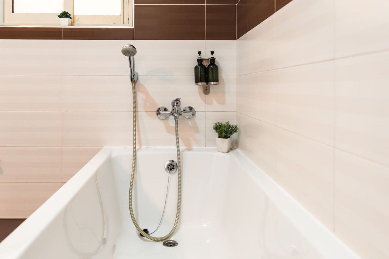 A bathroom with a bathtub, a handheld showerhead, and two wall-mounted soap dispensers.