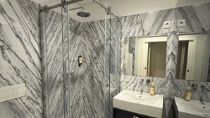 Un bagno con pareti in marmo, cabina doccia in vetro, un water e due lavandini con asciugamani.