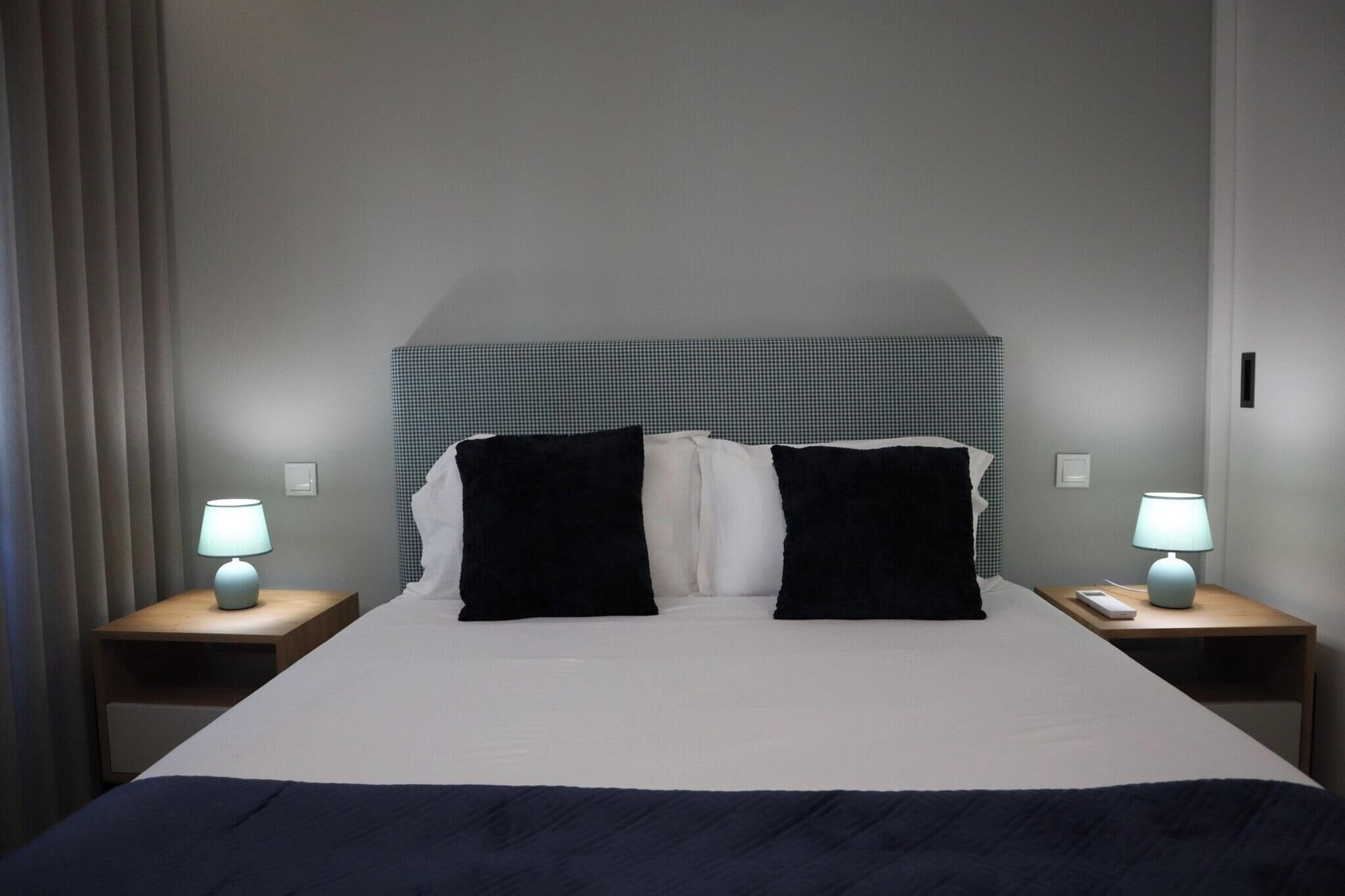 A hotel room with a bed, two bedside tables, and lamps.