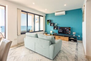 A modern living room with a sofa, a flat-screen TV, and a view of the sea through large windows. - De Redin Collection / Suite No.11 / Ocean Views (Sliema)