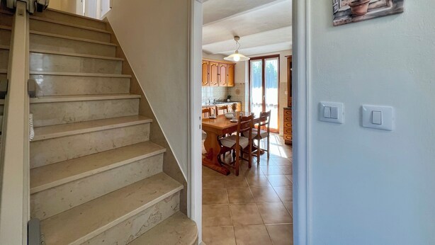 Una escalera conduce a una cocina con armarios de madera y un comedor.