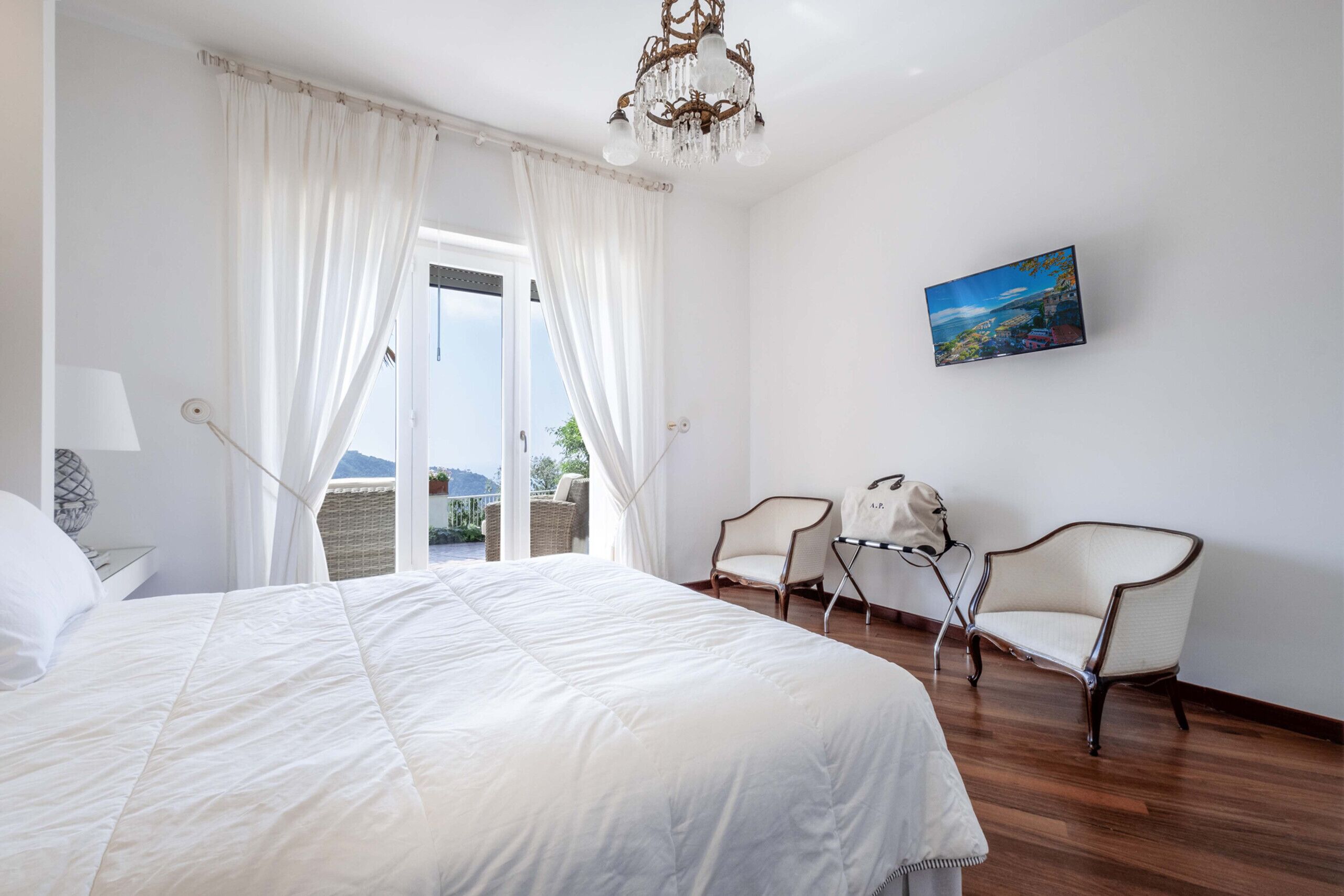 Une chambre avec un grand lit, deux fauteuils, un tableau et une vue sur l’extérieur.