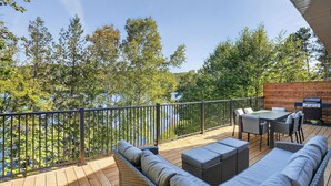 Une terrasse dotée de mobilier d’extérieur, d’un barbecue et offrant une vue sur un lac entouré d’arbres.