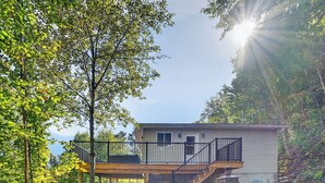 Une maison à deux étages avec une terrasse, entourée d’arbres et sous un ciel dégagé.