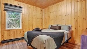 Une chambre aux murs lambrés, avec un lit, une fenêtre et un radiateur.