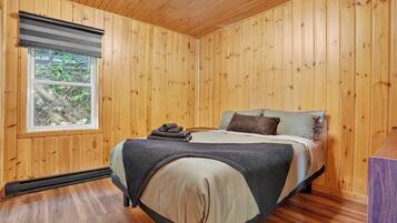 Een slaapkamer met houten lambrisering, een bed, een raam en een verwarming.