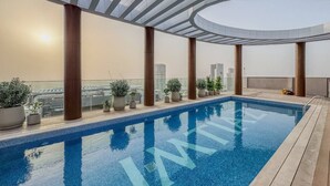 En pool på taget med frit udsyn over byens skyline, omgivet af plantekasser og moderne arkitektur.