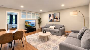 Ein modernes Wohnzimmer mit einem grauen Sofa, einem runden Couchtisch und einem Fernseher.
