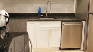 Una cocina moderna con armarios blancos, un refrigerador de acero inoxidable, un horno empotrado y un lavamanos con grifo.