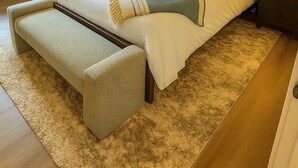 Un dormitorio ordenado con una cama grande, mesitas de noche con lámparas, un banco y una ventana con cortinas.