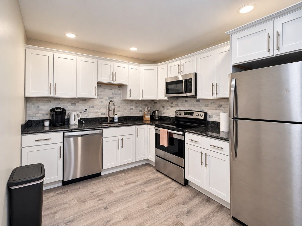 A modern kitchen with white cabinets, stainless steel appliances, and a black countertop.