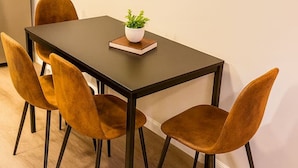 Un comedor con una mesa rectangular, cuatro sillas, una planta en maceta y un interruptor de luz en la pared.