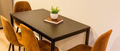 Un comedor con una mesa rectangular, cuatro sillas, una planta en maceta y un interruptor de luz en la pared.