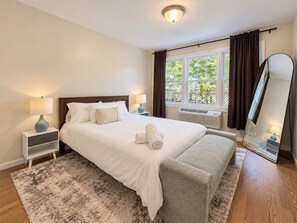A hotel room with a bed, bedside tables, a large mirror, and a window with curtains.