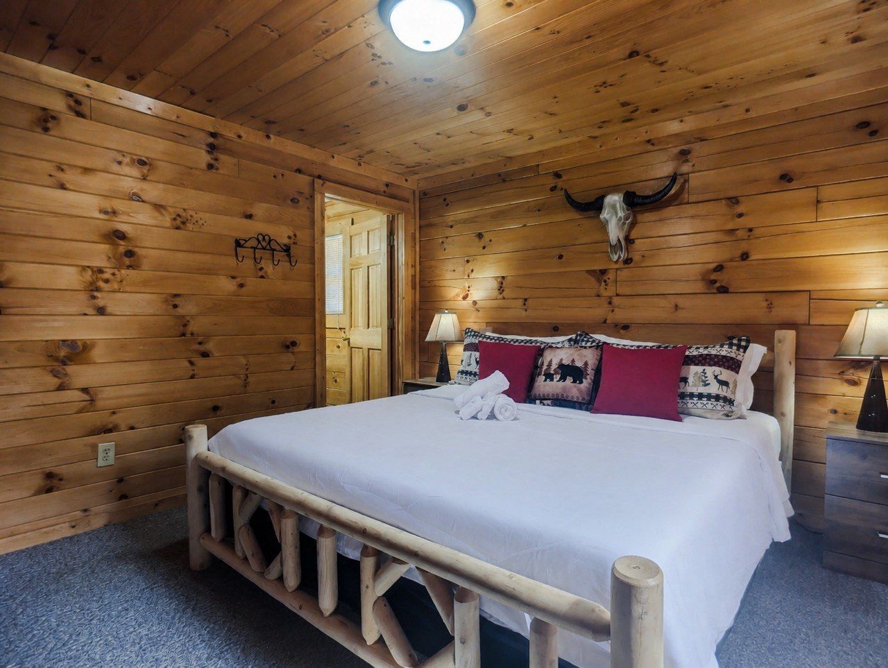 A wooden cabin room with a bed, a door, and a wall-mounted cow skull decoration.